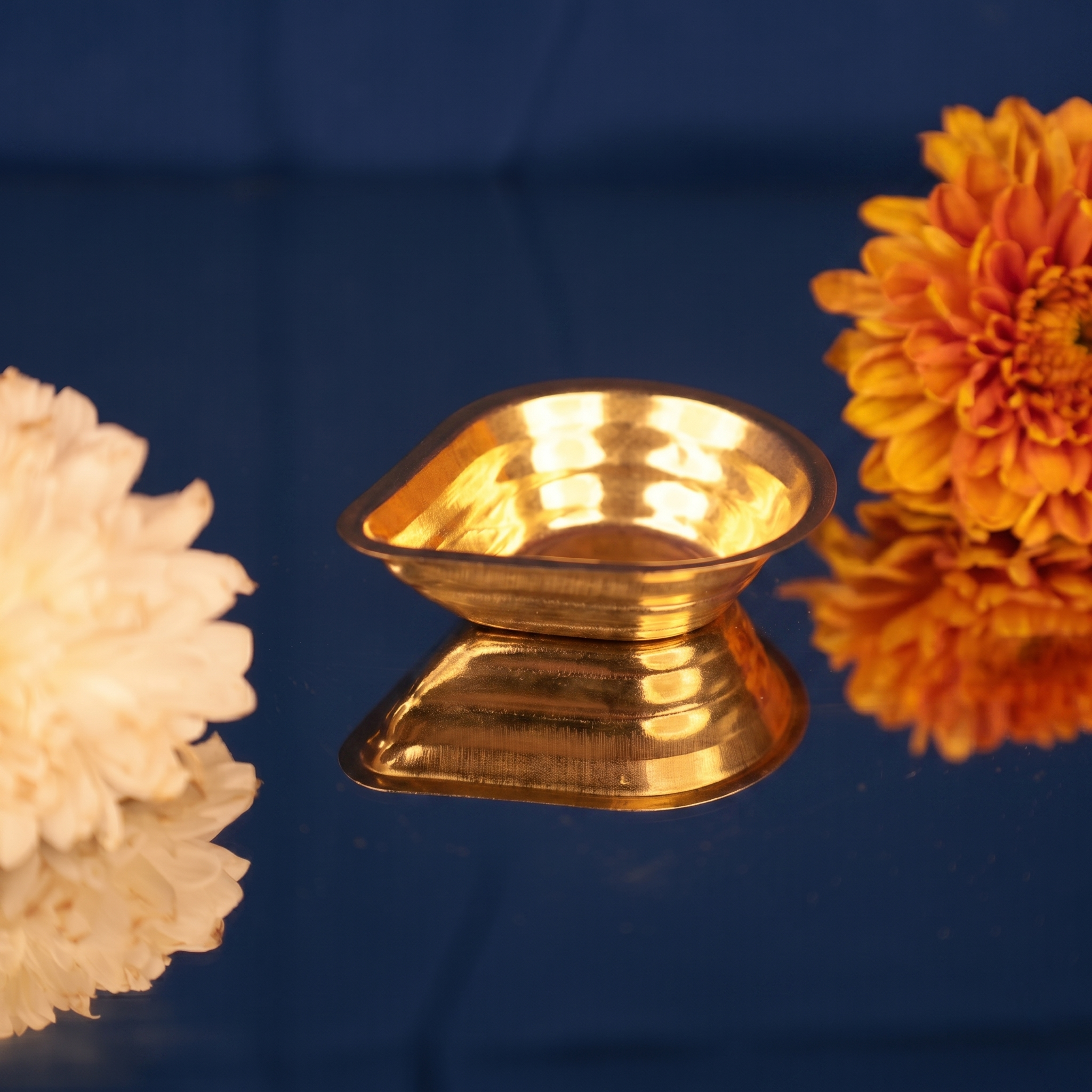 Agal Vilakku in a slight top-angle right-side view on a reflective blue surface with white and orange flowers against a blue backdrop