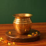 Kalash Sombu in front view on a round wooden base with scattered marigold petals against a deep green background