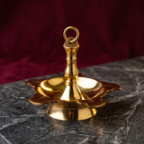 Thookku Vilakku hanging lamp with ring hook and scalloped base in a slight top-angle front view on a marble surface against a maroon backdrop