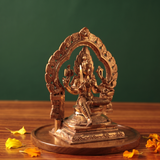 Maariamman idol on the left side angle with floral arch prabhavali seated on an engraved base with yellow and orange petals on a wooden plate.
