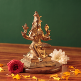 Raja Rajeshwari idol on the left side angle, seated with four arms, with red and white flowers and scattered petals on a wooden plate.