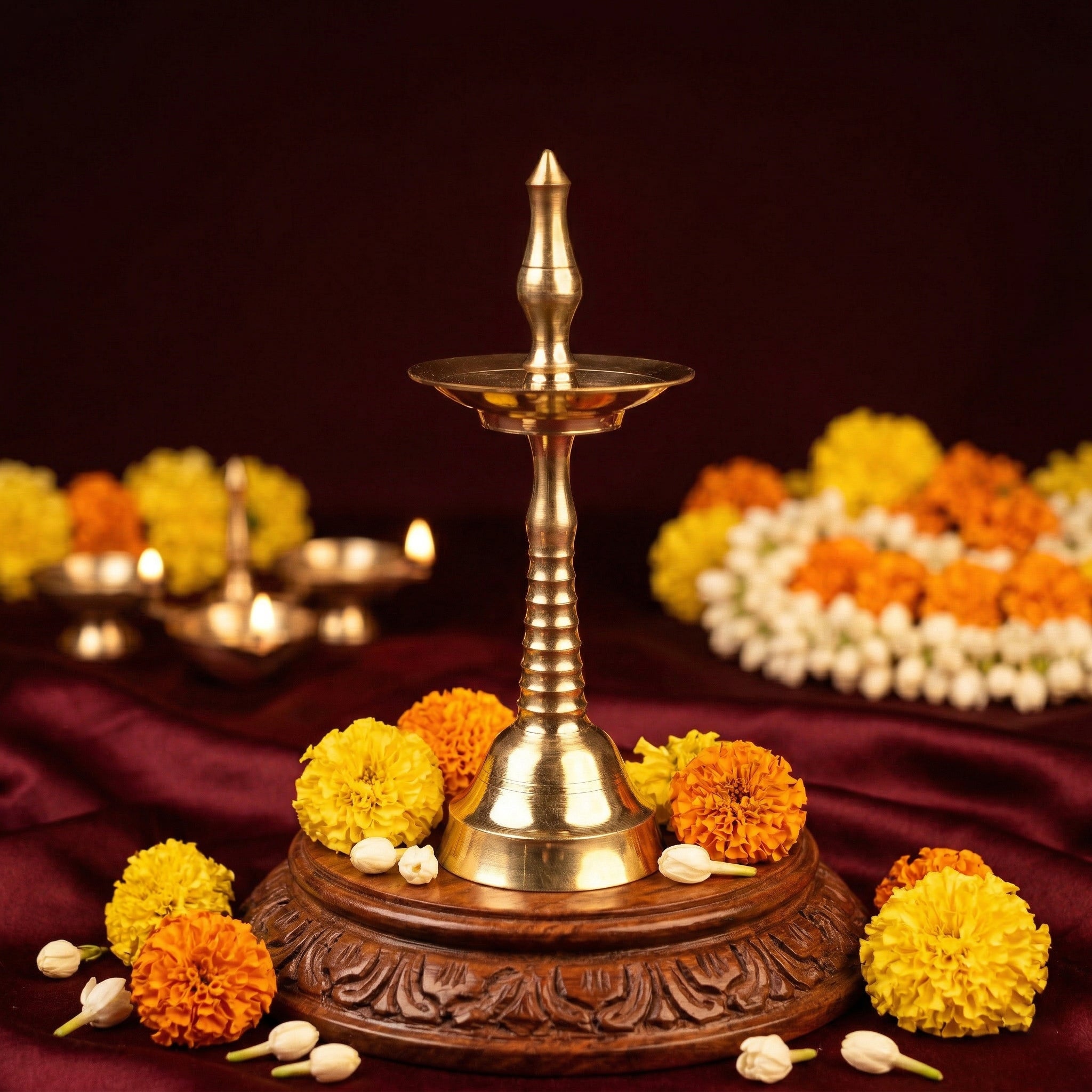 Nilavilakku Kerala floor lamp in a slight top-angle view on a carved wooden base with marigold and jasmine flowers against a maroon backdrop