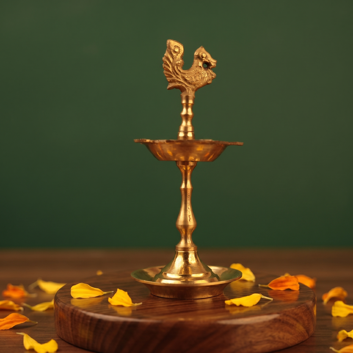 Karaikudi Vilakku with left-facing peacock on top in front view on wooden base with colorful petals against green backdrop