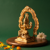 Maariamman idol in right side angle with leafy arch prabhavali seated on lotus base with white flower and scattered petals on a wooden plate.