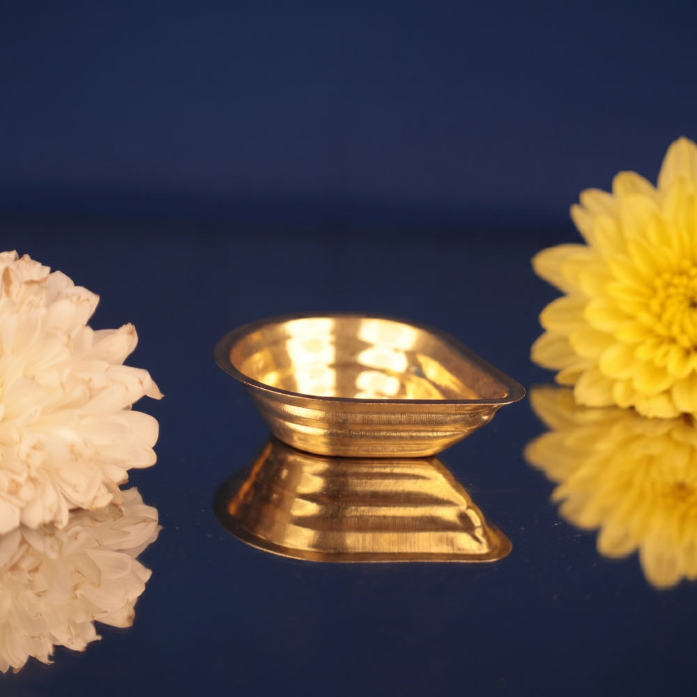 Agal Vilakku in a slight top-angle left-side view on a reflective blue surface with white and yellow flowers against a blue backdrop