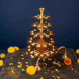 Aal Vilakku Adukku Aarthi with seven tiers in a slight top-angle view with yellow and orange flowers on a stone surface against a blue backdrop