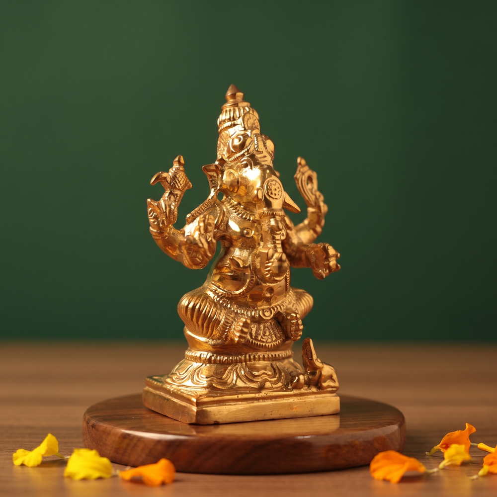 Ganesh Sitting Edampuri in the left side angle, seated with four arms, with scattered yellow and orange petals on a wooden plate.