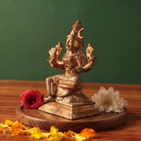 Raja Rajeshwari idol on the right side angle, seated with four arms, with red and white flowers and scattered petals on a wooden plate.
