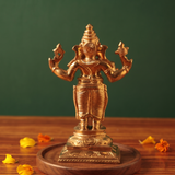 Ganesh Standing Valampuri in back view with four arms raised on an engraved base with scattered yellow and orange petals on a wooden plate.