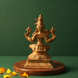 Raja Rajeshwari idol in back view, seated with four arms on an engraved base with yellow petals on a wooden plate.