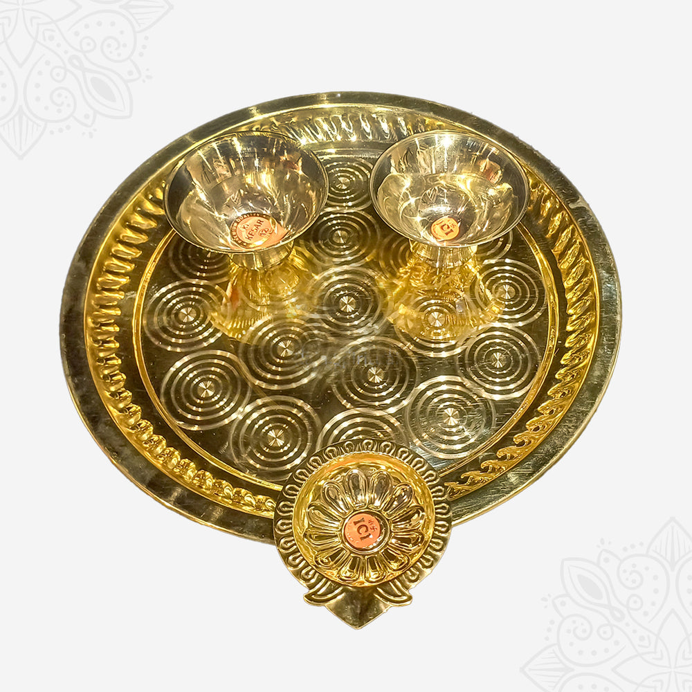 Aarti plate with two bowls and floral diya shown in slightly low top-down wider view with circular engraved border against white backdrop.