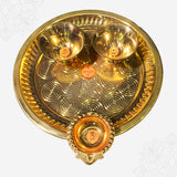 Aarti plate with two bowls and a diya shown in top-down view with circular engraved design against white backdrop.