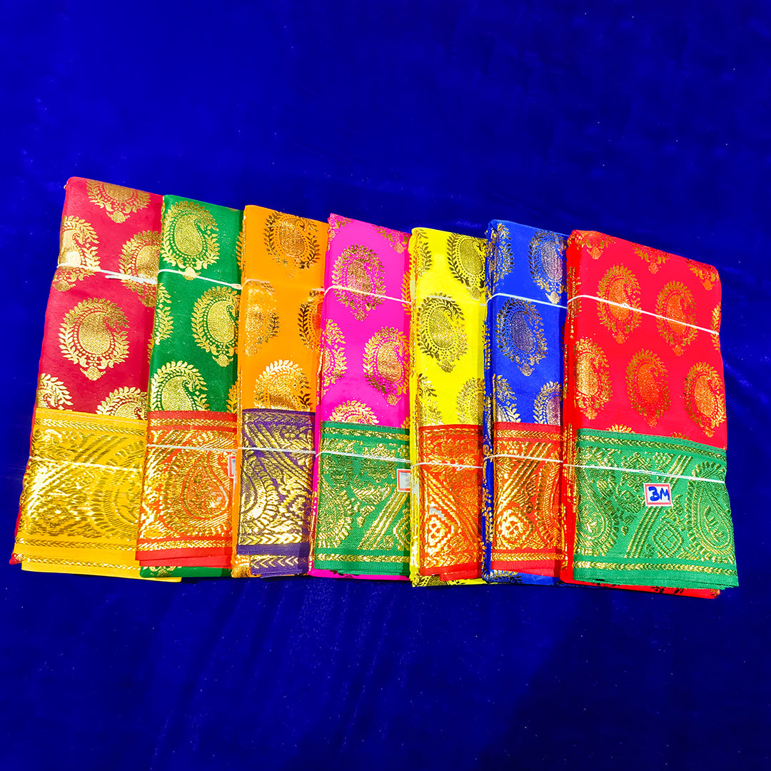 Seven folded Amman sarees in green, dark yellow, orange, red, blue, rose, and yellow with gold zari design placed flat on a blue velvet surface.