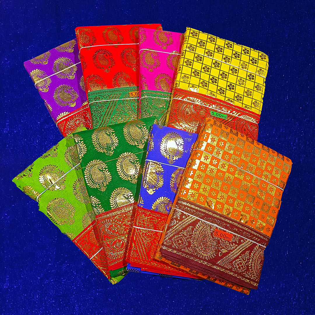 Eight folded Amman sarees in yellow, rose, red, maroon, dark green, light green, blue and dark yellow with gold zari design placed on blue velvet surface.