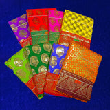 Eight folded Amman sarees in yellow, rose, red, maroon, dark green, light green, blue and dark yellow with gold zari design placed on blue velvet surface.