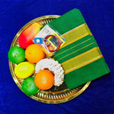Top view of green amman saree 9 gajan in a gold plate with fruits and flower garland on blue surface
