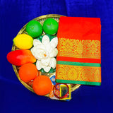 Top view of orange amman saree jacquard with gold zari print in a gold plate with fruits and lotus flower on blue surface
