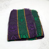 Bedsheet Nelson folded in purple and green floral jacquard pattern with gold stripes on white surface, slight top-down angle view