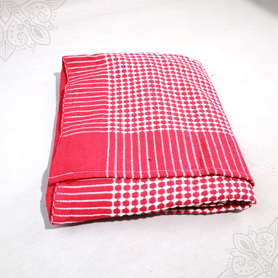 Bedsheet folded in red and white dot and stripe cotton pattern on white surface, slight top-down angle view