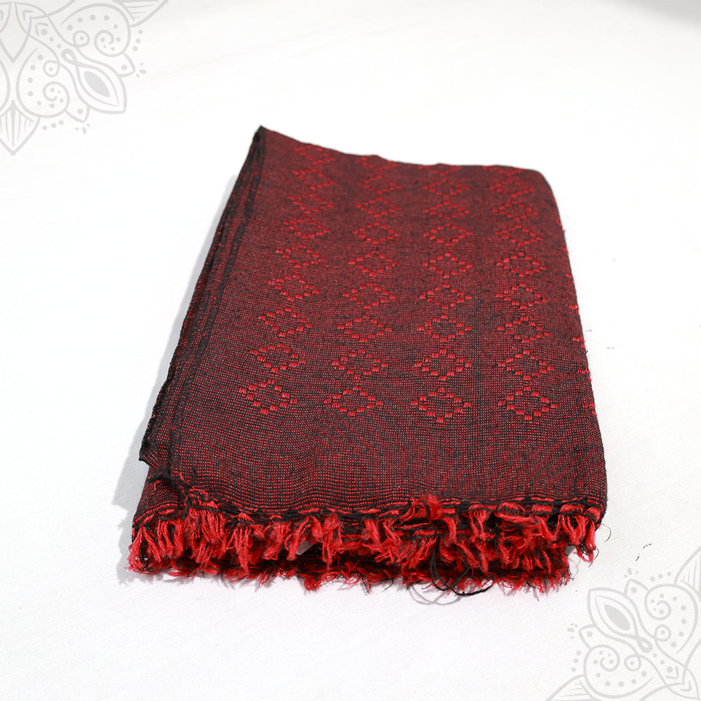 Bedsheet Nuton folded in dark red and black diamond woven pattern with red fringed edge on white surface, slight top-down angle view