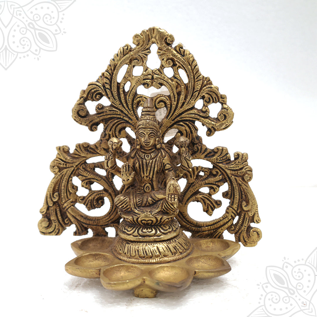Fancy Lakshmi frame with six-faced vilakku seated on a lotus with ornate floral prabhavali in a straight front view against a white backdrop