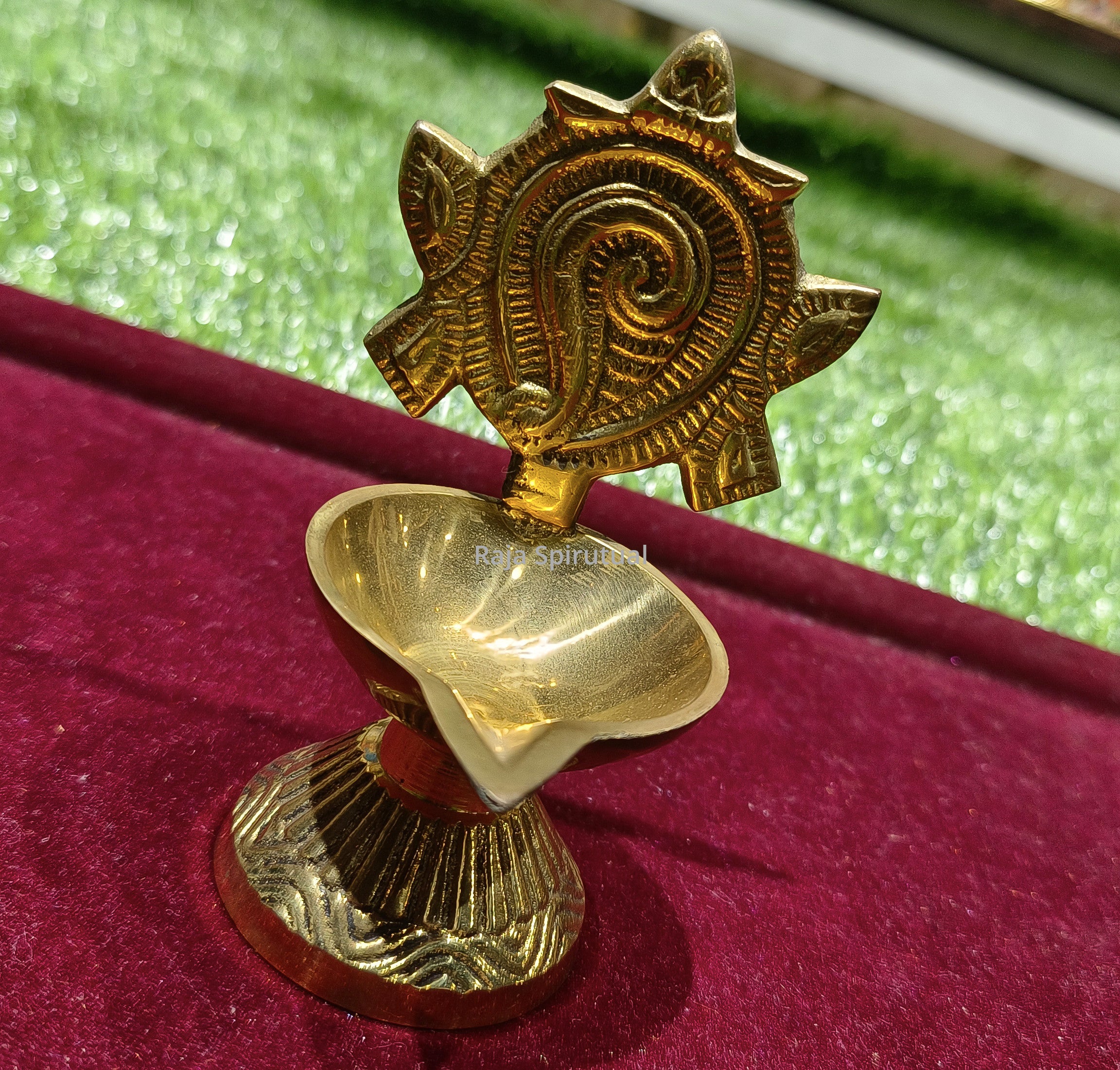 Fancy sangu vilaku slight top left view with conch spiral disc petal oil cup on ribbed round base on red velvet surface
