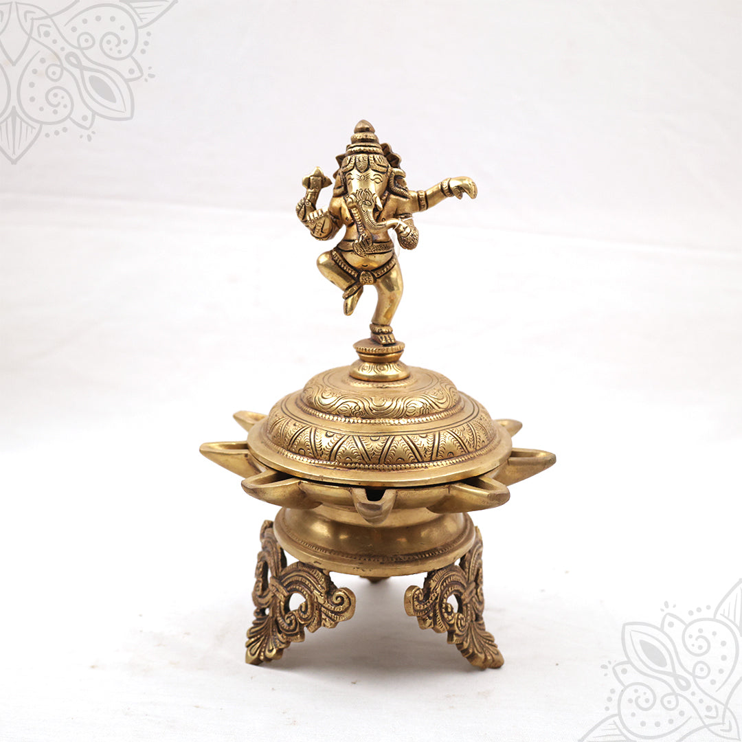 Fancy Vinayagar Vilakku with dancing Ganesha on top on engraved domed lamp with ornate stand in a straight front view against a white backdrop