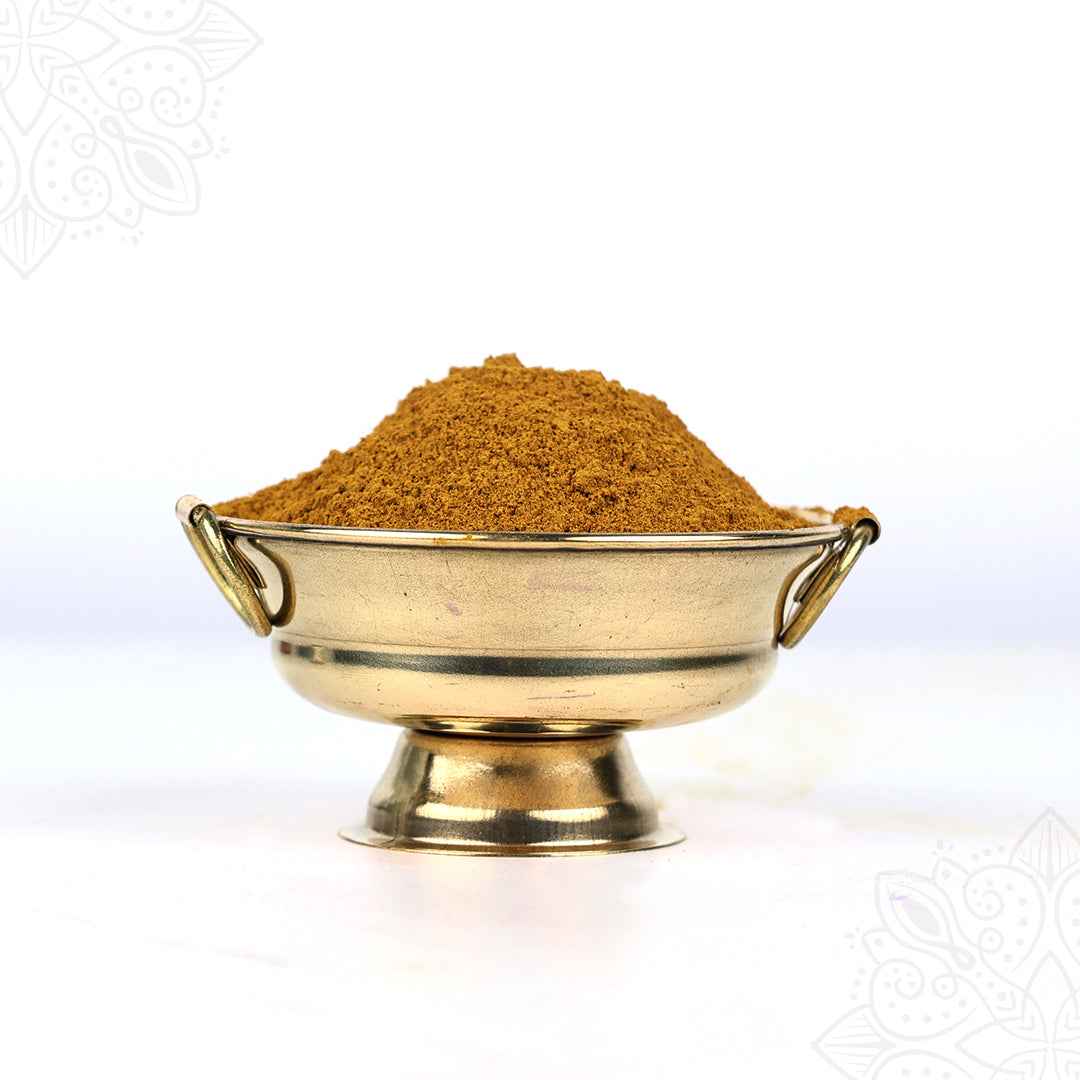 Slight right side view of kadhamba powder heaped in a brass uruli bowl with ring handles on white surface