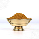 Slight right side view of kadhamba powder heaped in a brass uruli bowl with ring handles on white surface