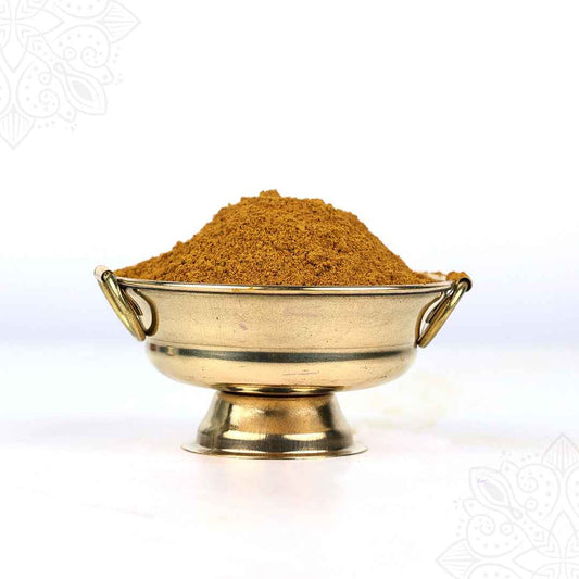 Front view of kadhamba powder heaped in a brass uruli bowl with ring handles on white surface