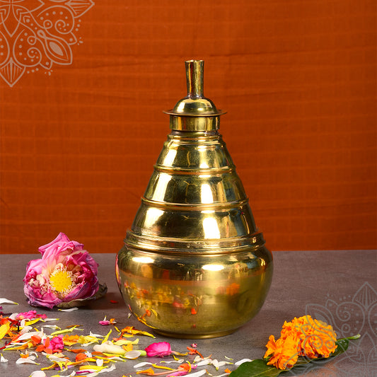 Kumba aarti plain small single piece with smooth tiered top, lotus and marigold flowers beside, straight front view on orange backdrop