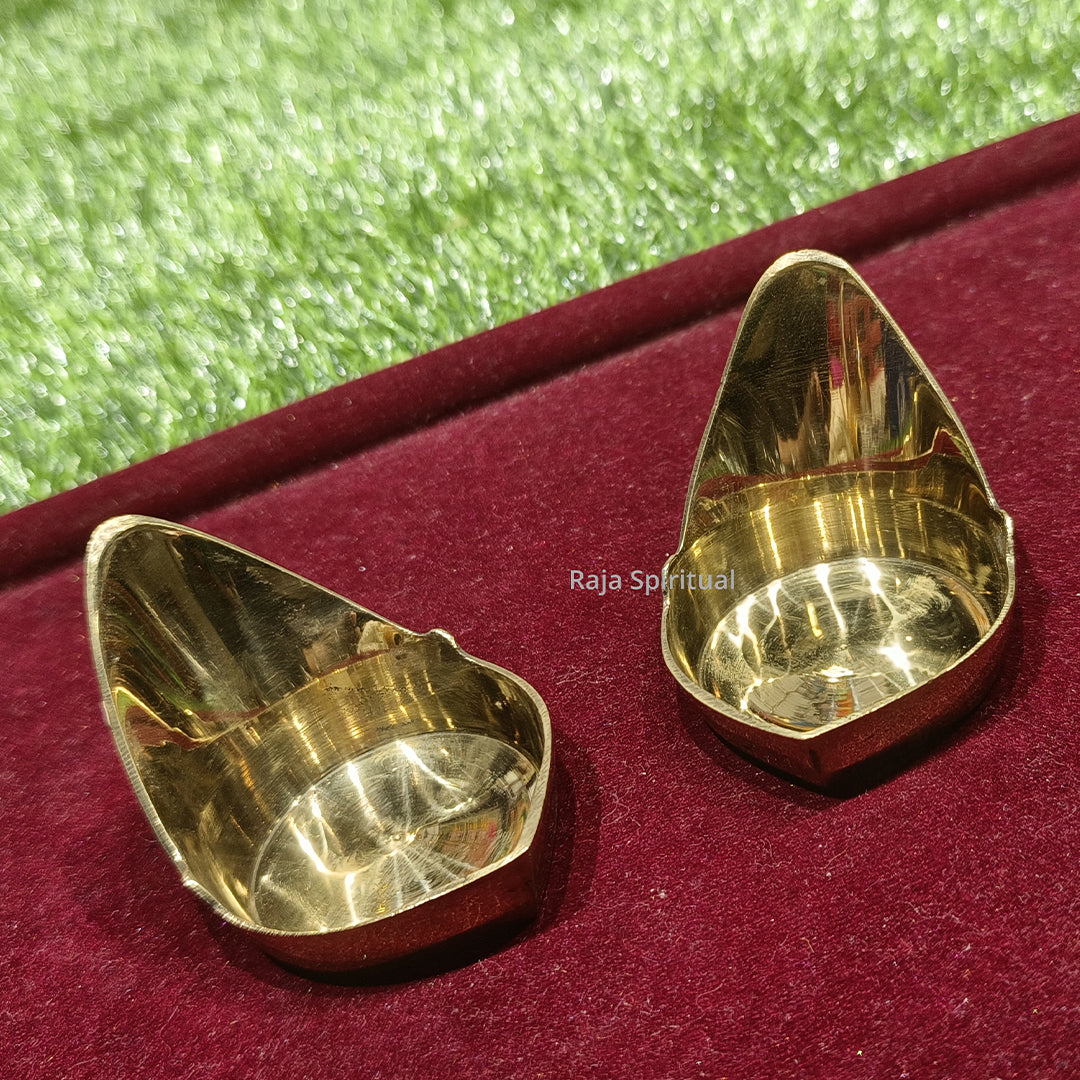 Two maada vilaku top left diagonal low view with triangular oil cup interiors side by side on red velvet surface
