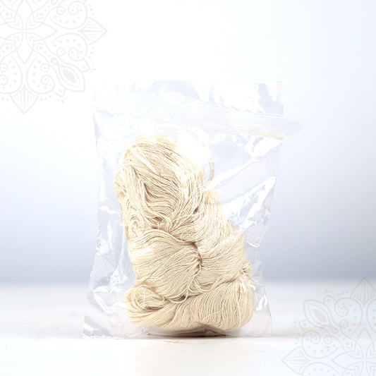 Front view of mangalya nool, white cotton thread bundle, packed in a clear plastic bag on a white surface