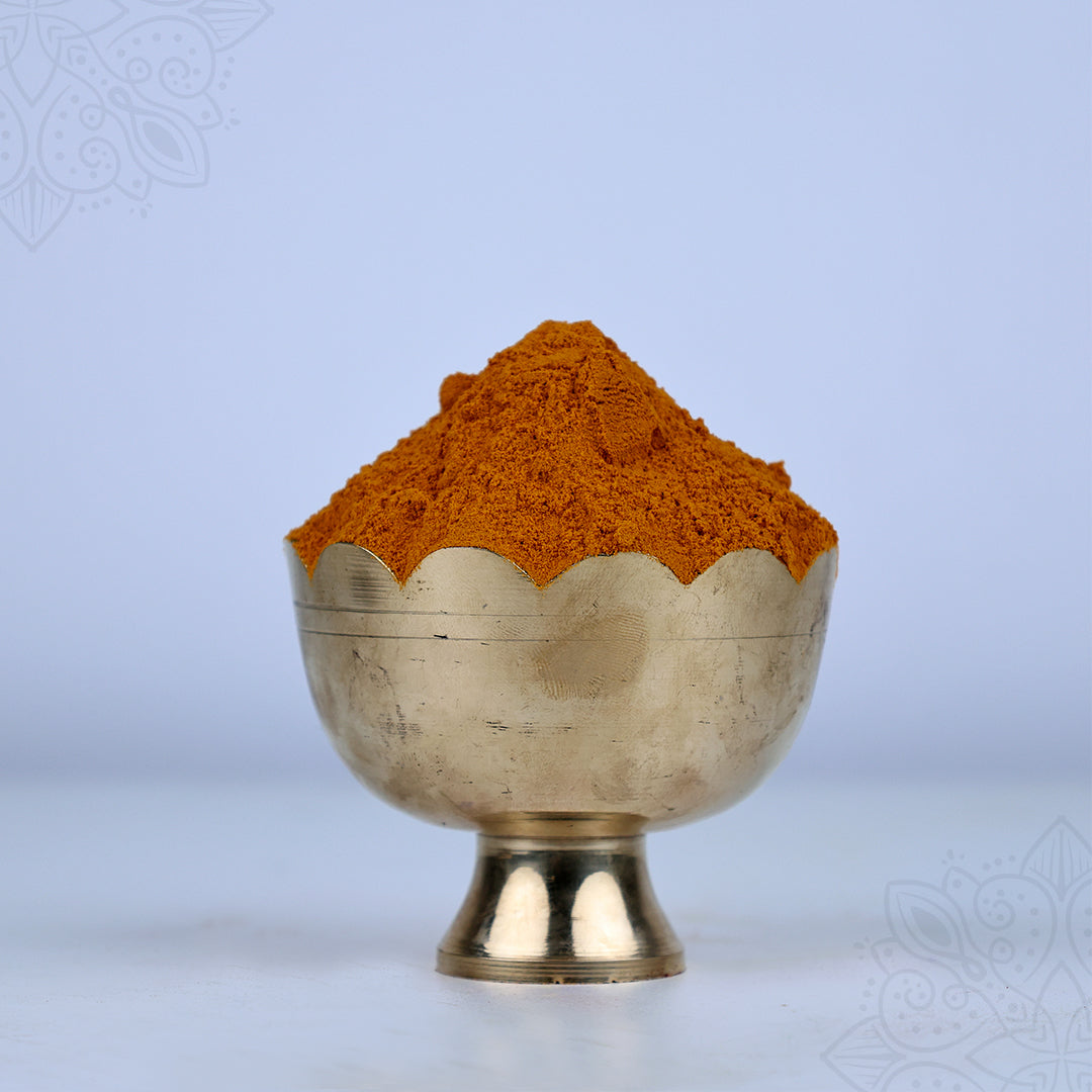 Manjal powder heaped in a scallop-edged puja bowl shown in straight front view with full base visible against a light blue backdrop.