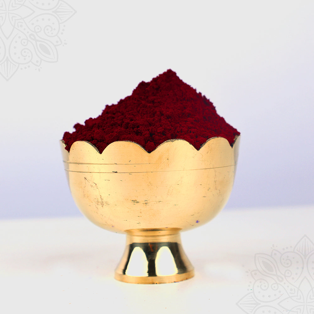 Maroon kumkum straight front view zoomed in showing deep red sacred powder heaped in golden scalloped bowl on pedestal for pooja use