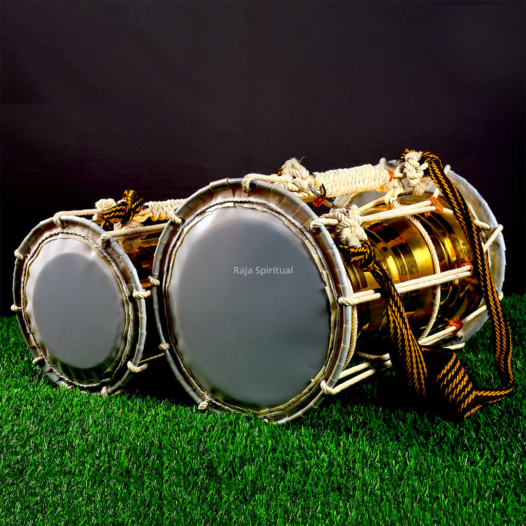 Pair of pambai leather drums placed on grass in a slight left side angle view showing both drum faces with white rope and gold braided cord against a dark backdrop