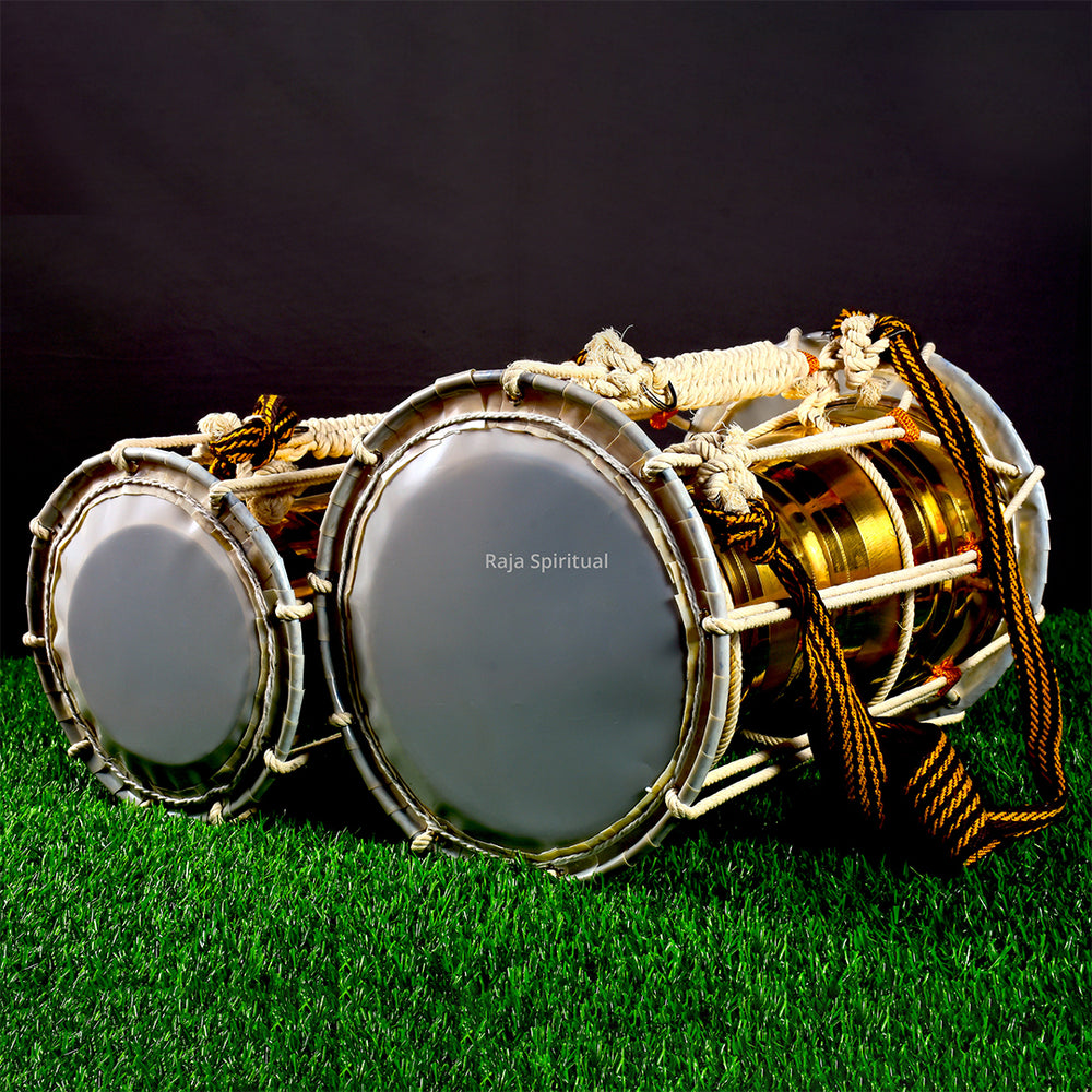 Pair of pambai leather drums placed on grass in a slight left side angle view showing both drum faces with white rope and gold braided cord against a dark backdrop