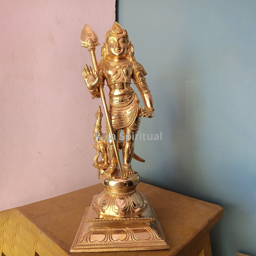 Panchaloga Bala Murugar standing with vel and peacock, on pedestal base, wooden table against pink and blue wall, straight front view