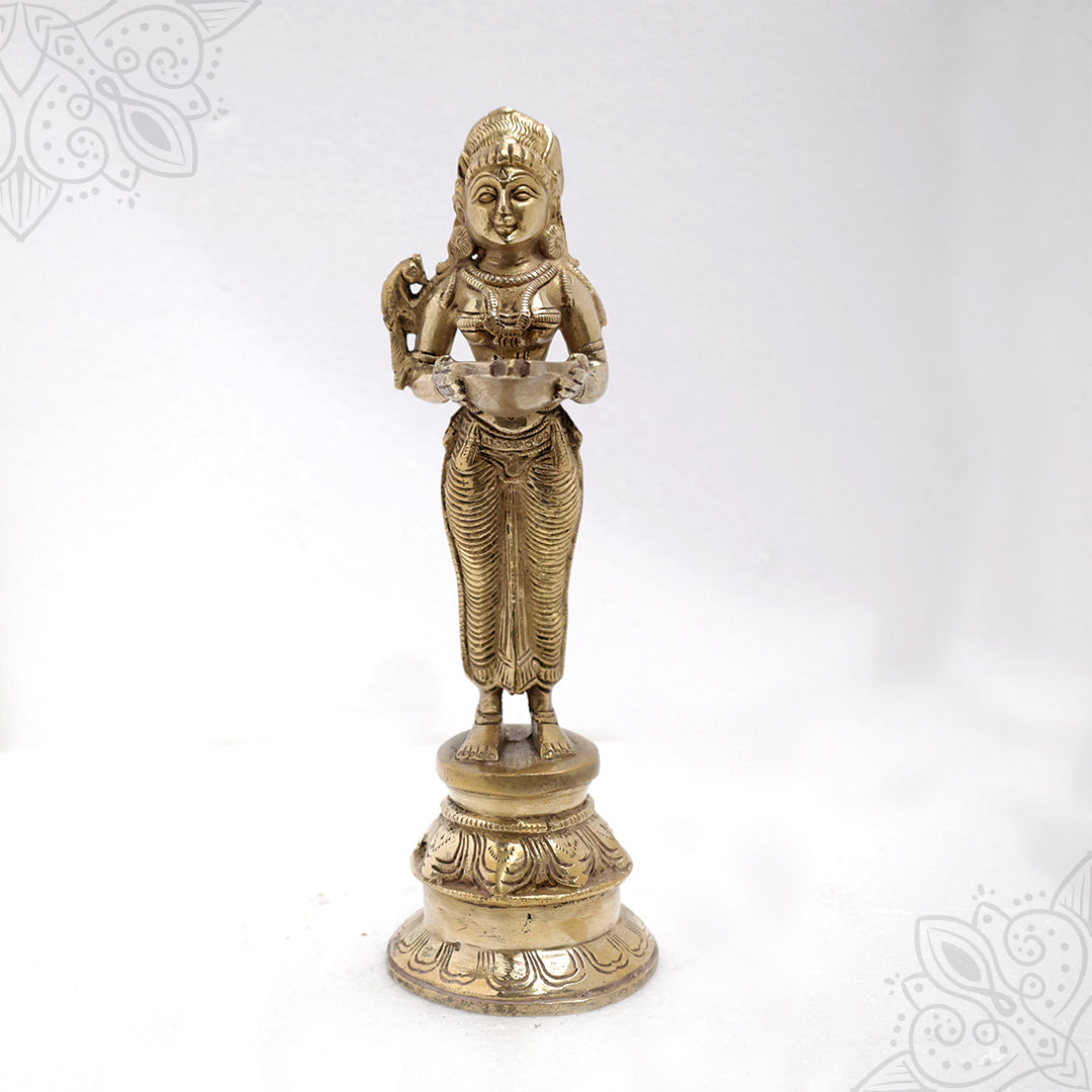 Pavai Vilakku standing goddess holding a diya with a bird on her shoulder on a lotus base in a straight front view against a white backdrop