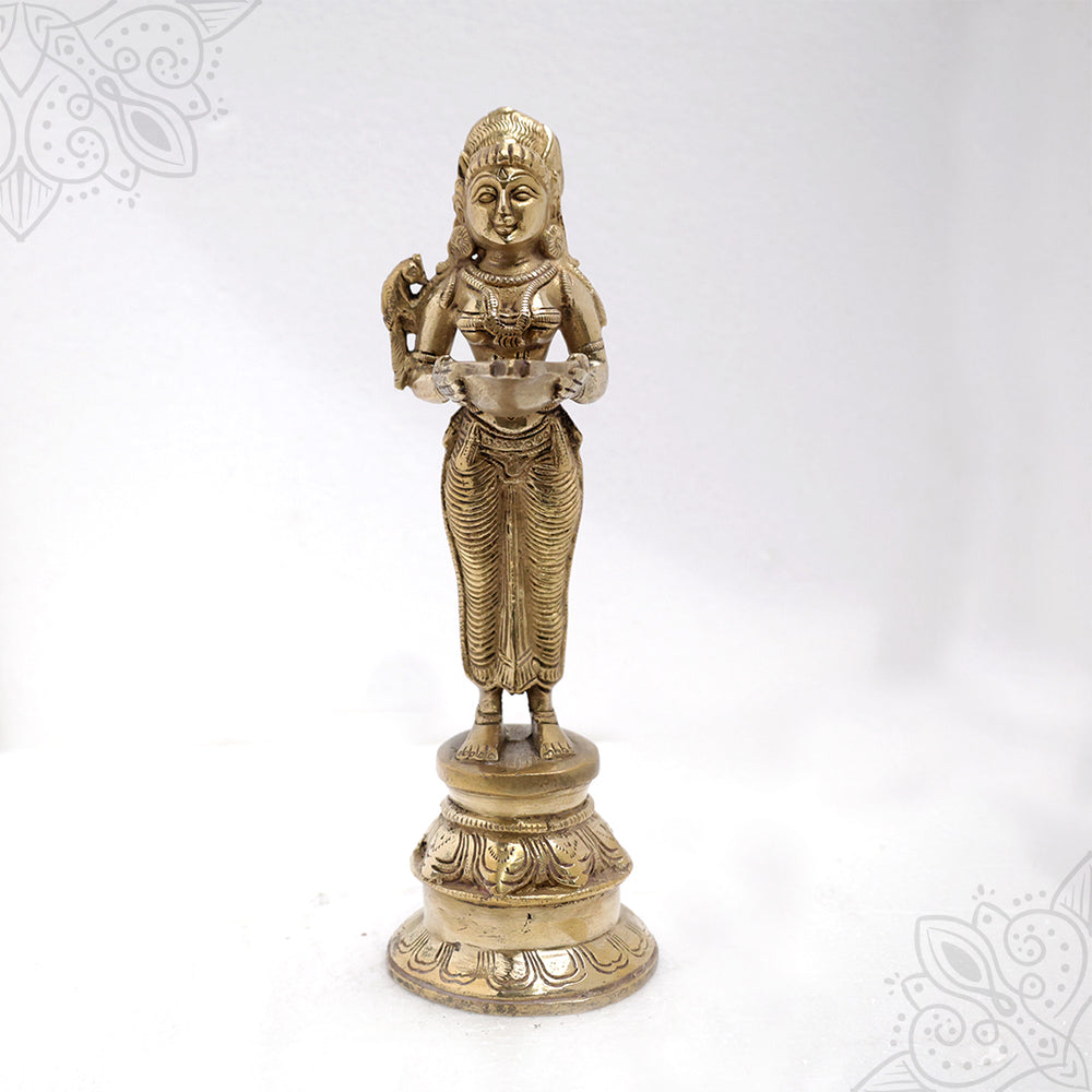 Pavai Vilakku standing goddess holding a diya with a bird on her shoulder on a lotus base in a straight front view against a white backdrop