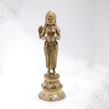 Pavai Vilakku standing goddess holding a diya with a bird on her shoulder on a lotus base in a straight front view against a white backdrop