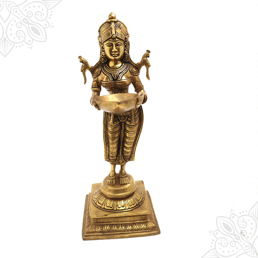 Pavai Vilakku standing goddess holding a diya with two parrots on her shoulders on a square lotus base in a straight front view against a white backdrop
