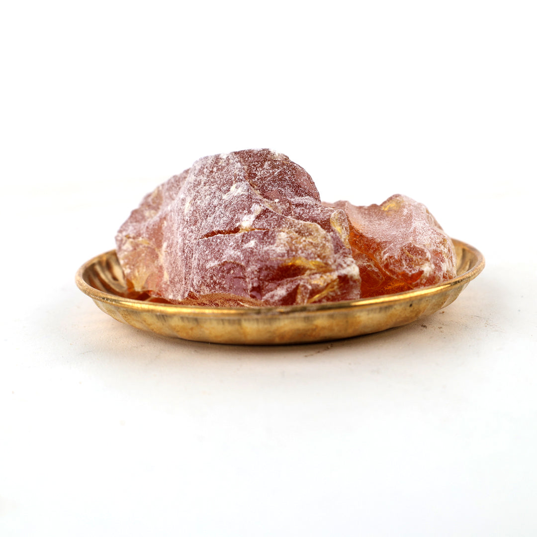 Rowsanam katti resin chunks placed in a small golden pooja plate against a white background, straight front view