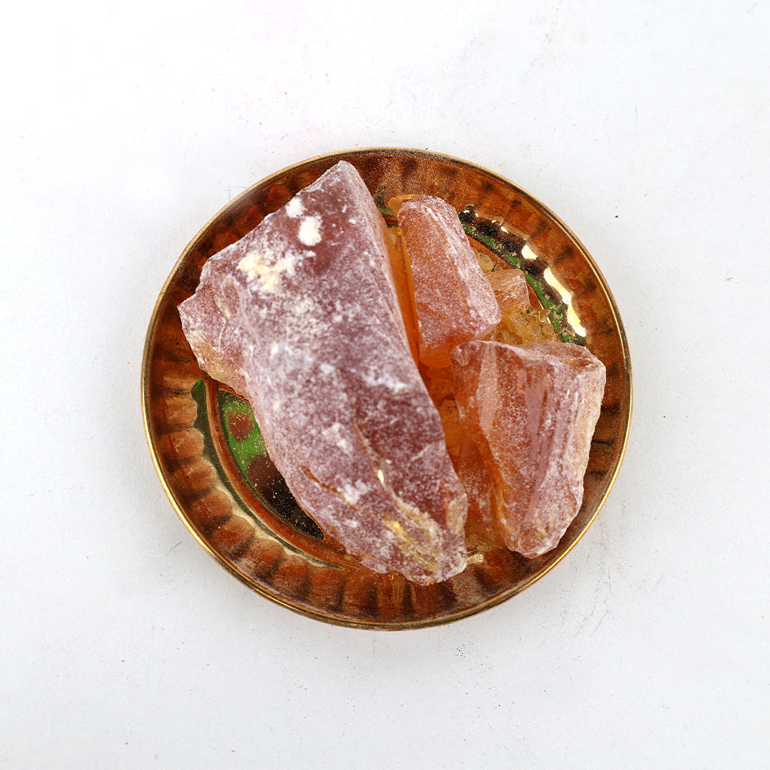 Rowsanam katti resin pieces arranged in a golden ribbed pooja plate on white surface, top-down view