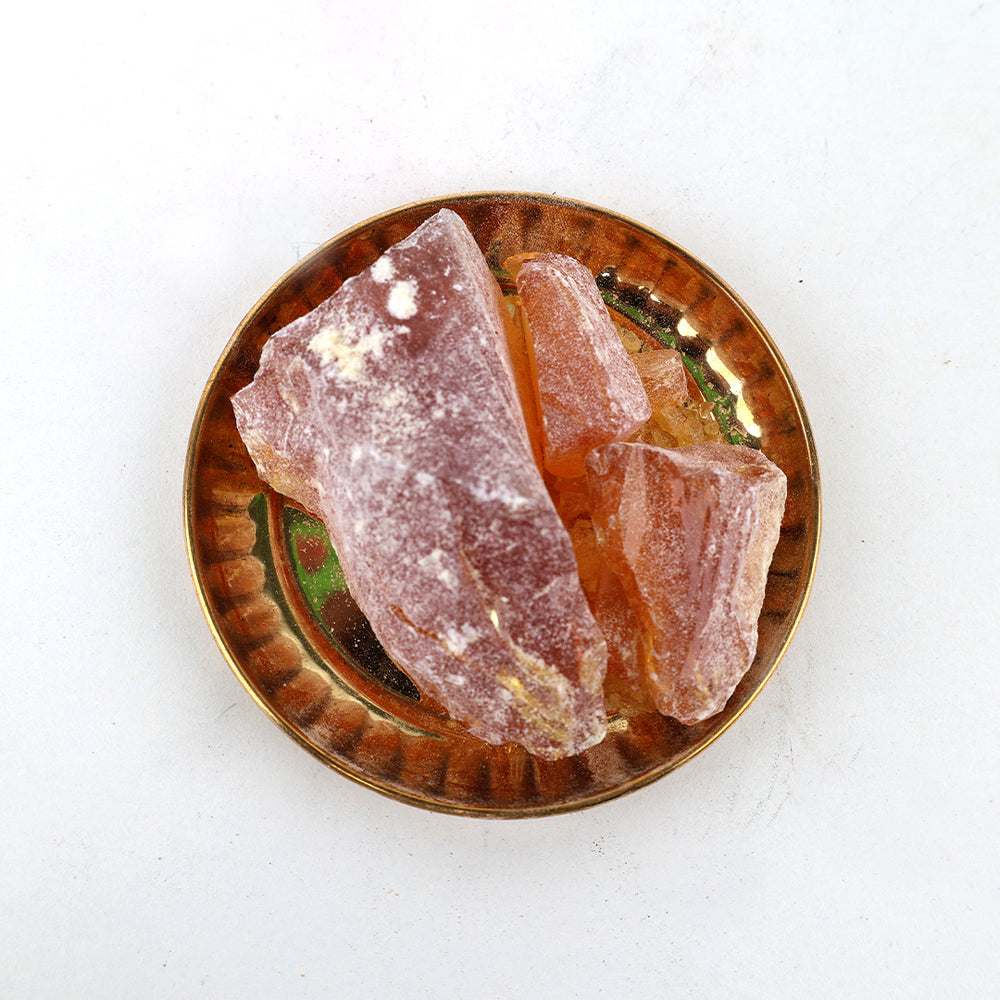 Rowsanam katti resin pieces arranged in a golden ribbed pooja plate on white surface, top-down view