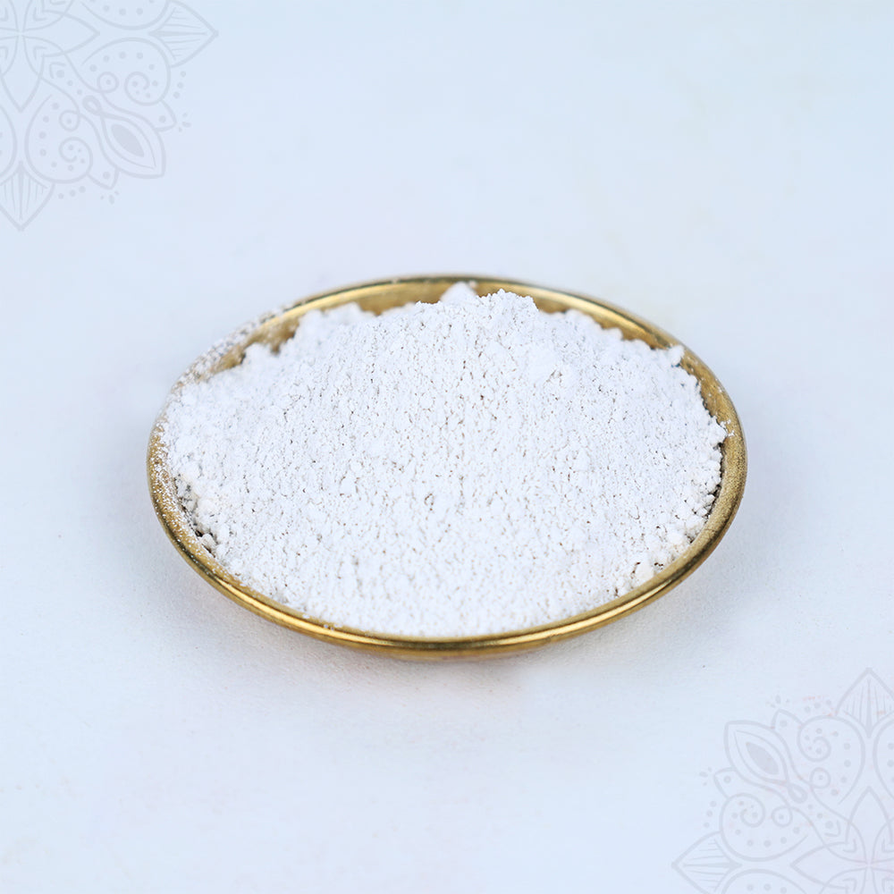 Slight top angle view of white thiruman powder placed in a round gold plate on white surface